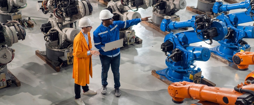 Two people in hard hats inspect robotic arms inside an industrial facility