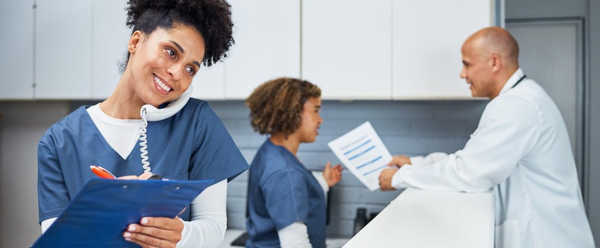 Healthcare staff member writes on clipboard while speaking on desk phone