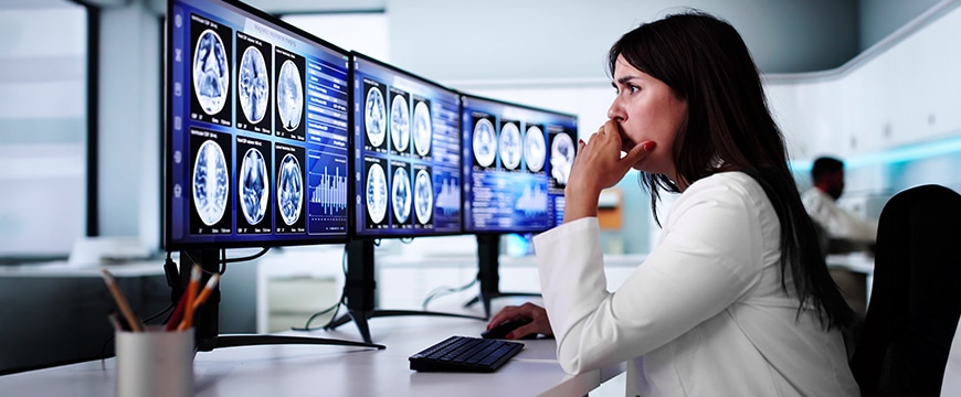 Healthcare professional reviewing medical information across multiple computer monitors.