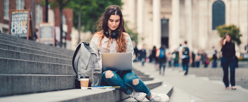 Young girl sitting at the steps and using lap top