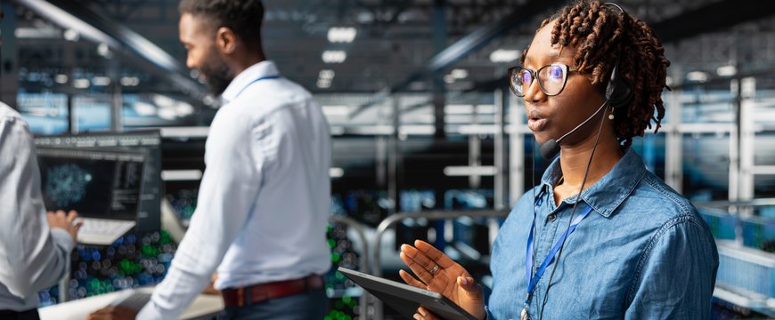 Person wearing headset and holding tablet in a technology operations center