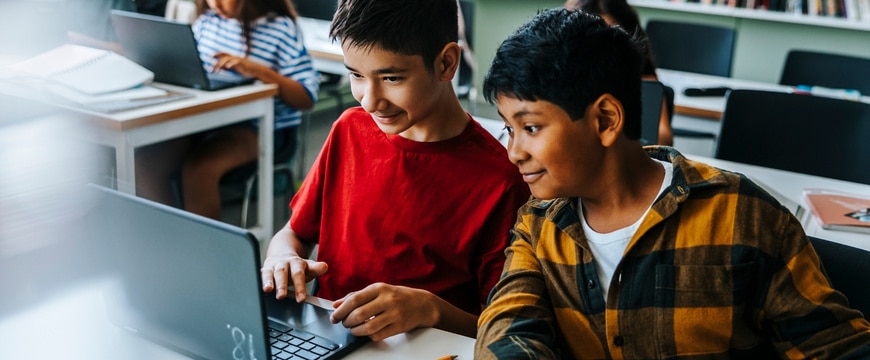 Two students work together on a laptop in a classroom