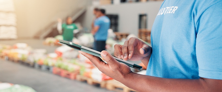 Volunteer, ngo and tablet with hands of man in warehouse for non profit, inventory checklist and distribution. Charity, social responsibility and food bank program with closeup of person for donation