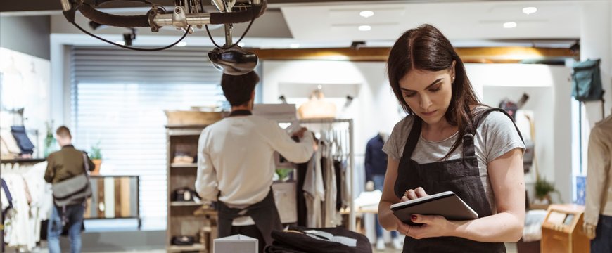 Retail employee reviewing information on a tablet beside folded clothing