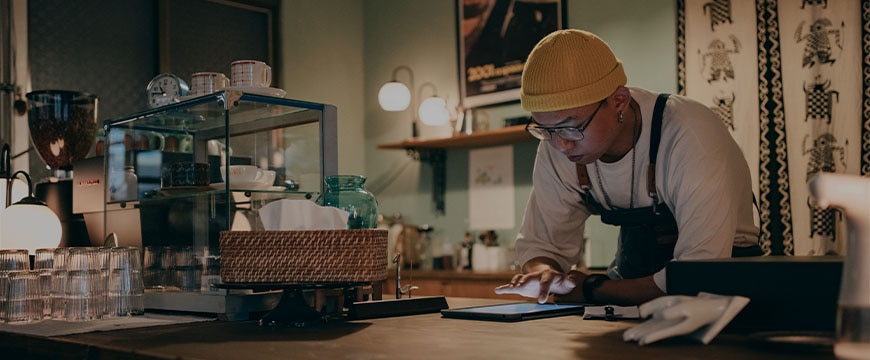 Cafe worker using tablet behind counter with glassware and coffee equipment