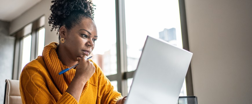 Person working at a desk using a laptop and holding a pen