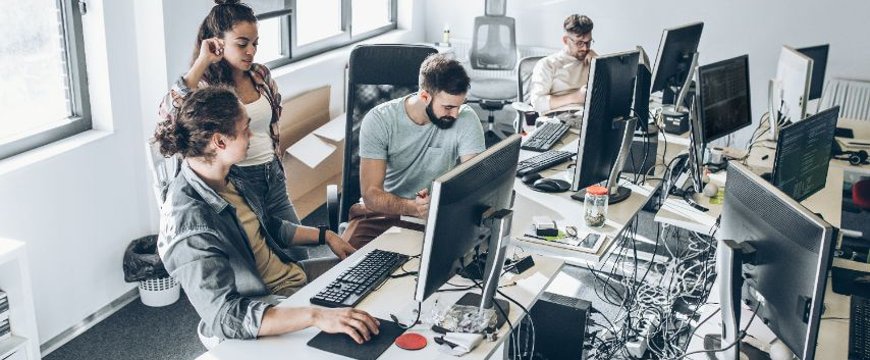 Office team working at desks with multiple monitors and visible cable clutter