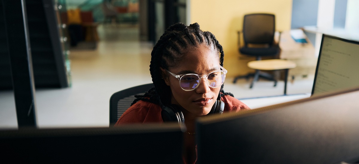 Professional focused on dual monitors in modern office workspace.