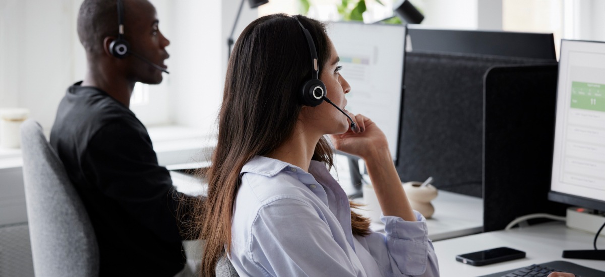 Support staff wearing headsets assist clients from computer workstations in an office.