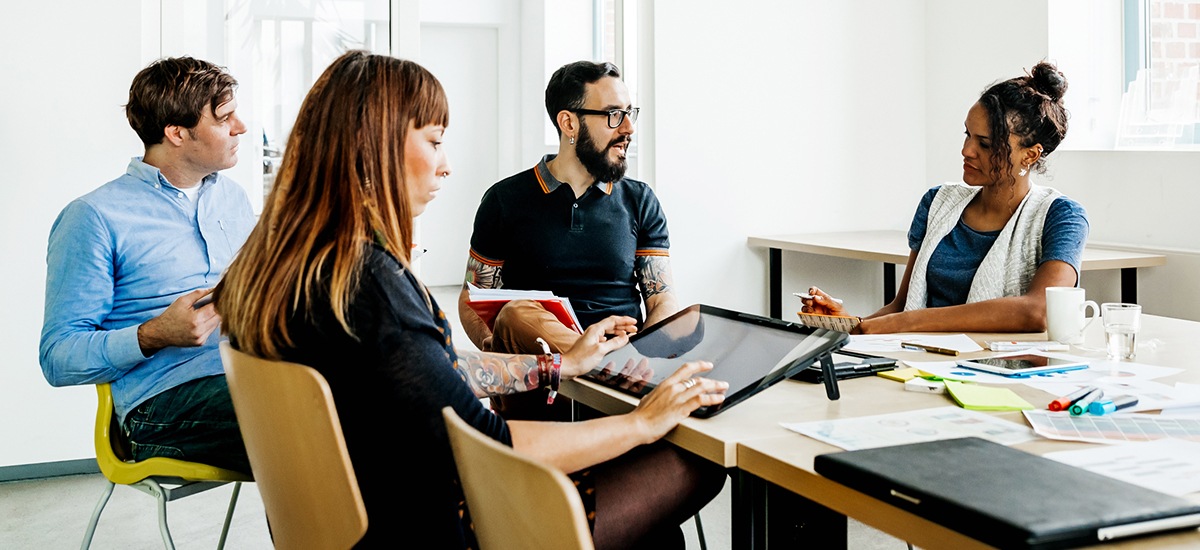 Four colleagues collaborating at a table with documents and a digital tablet in a meeting room.