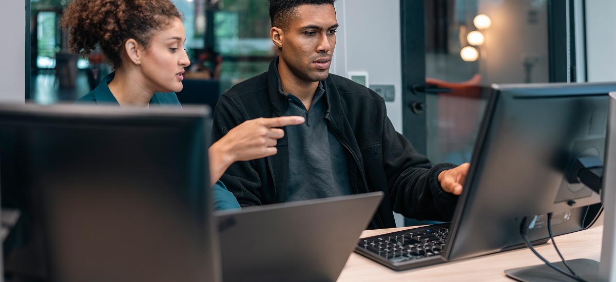 Two coworkers reviewing information on a desktop monitor in an office.