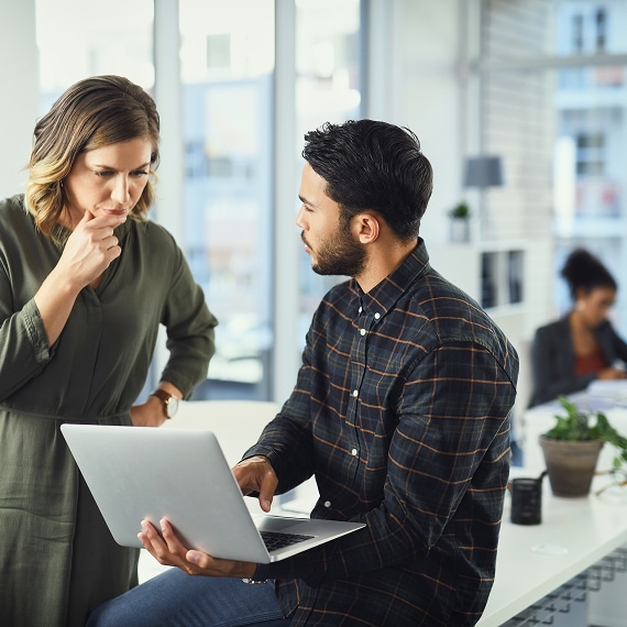 Two professionals reviewing data together on a laptop in modern office.