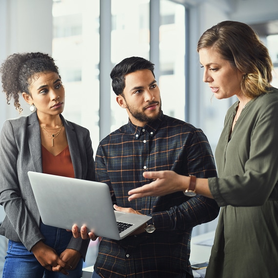 Three coworkers discussing project details while referencing laptop.