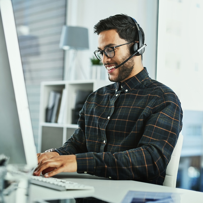 Man wearing headset smiling while working at desktop computer.