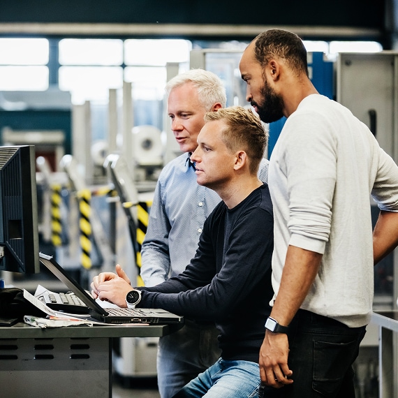 Three professionals reviewing data together on computer in industrial facility.