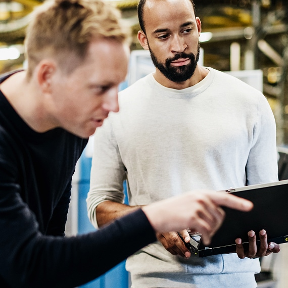 Two engineers discussing information displayed on laptop in plant.