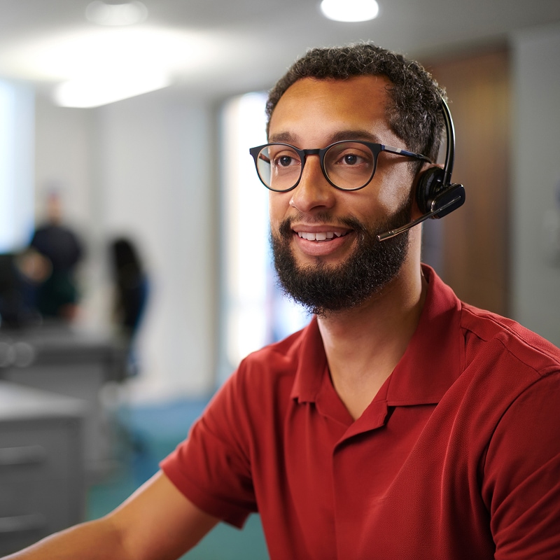 Customer support representative wearing headset smiling in office environment.