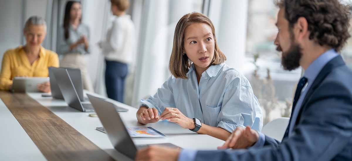 Two colleagues discussing data while reviewing a laptop in a bright office space.