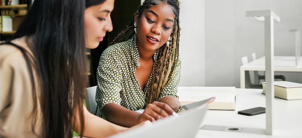 Two professionals reviewing information together on a laptop in a bright office setting.
