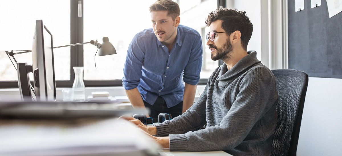 Two colleagues collaborating at a desktop computer in a modern workspace.