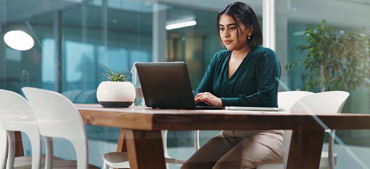 Professional working on a laptop at a table in a contemporary office environment.
