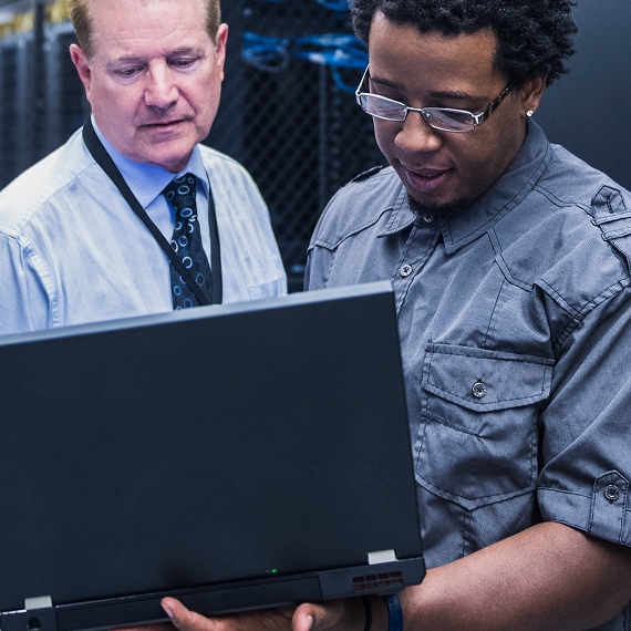 Two technicians examining laptop together in server room.