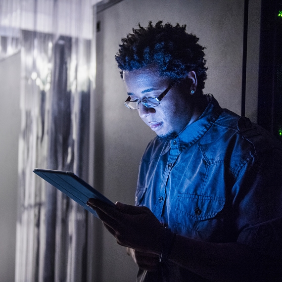 IT specialist checking tablet in dimly lit data center.