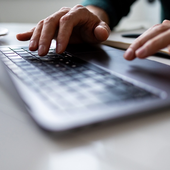 Hands typing on laptop keyboard at modern workspace.