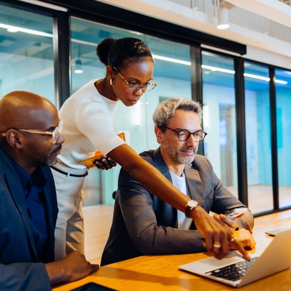 Colleagues review information together on a laptop in a modern office.