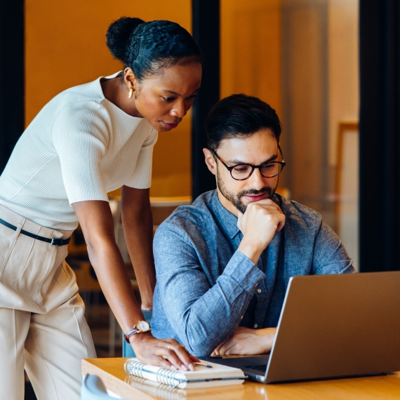 Two technology professionals review AI resources together on a laptop.