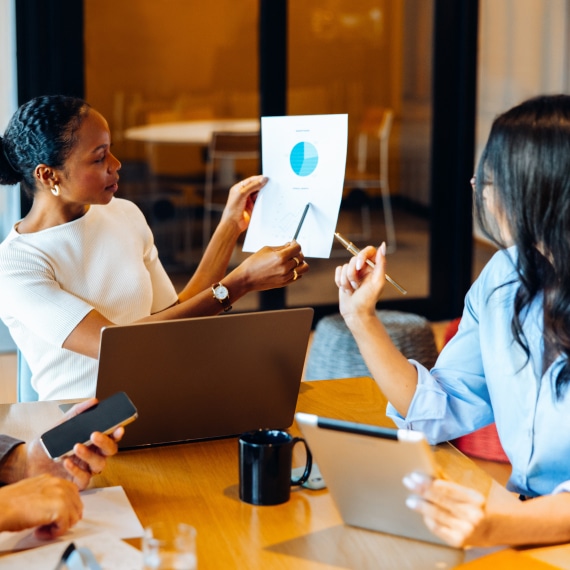 Colleagues collaborate on a laptop while discussing AI governance reporting.