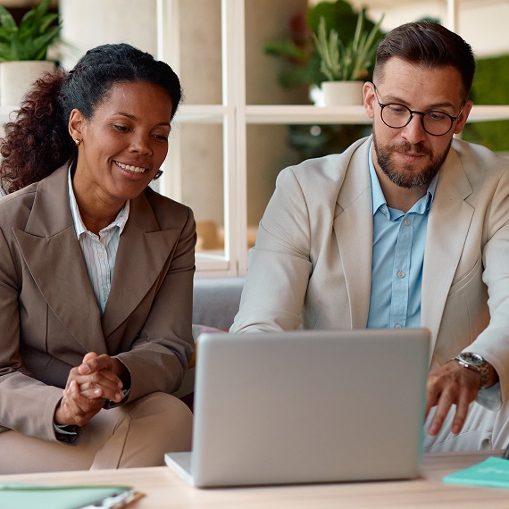 Two colleagues review data together on a laptop in a modern office.