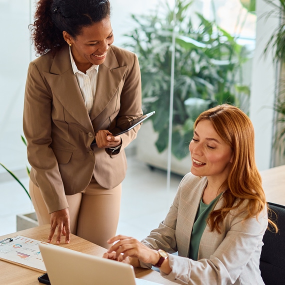 Two professionals collaborate at a desk reviewing reports and a laptop in a bright office.