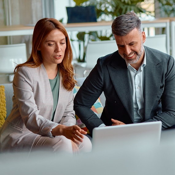 Two colleagues discuss strategy while reviewing a laptop in a modern office.