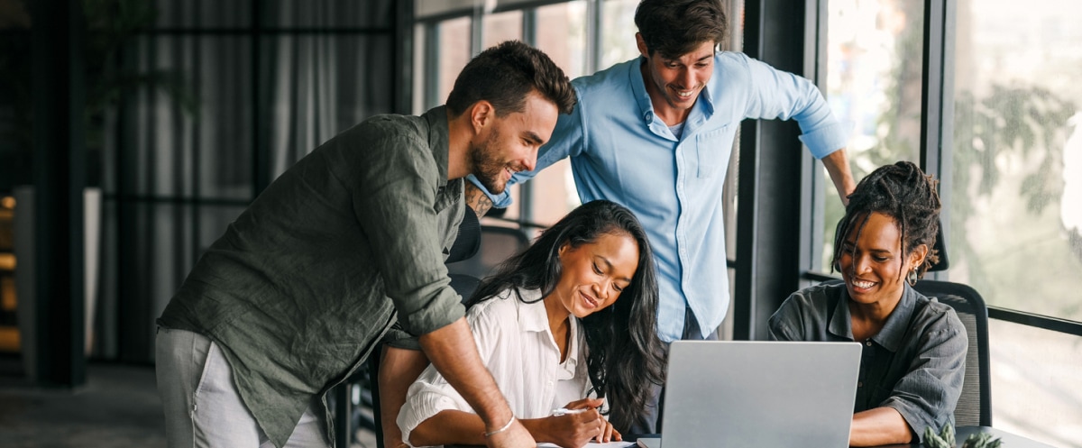 Four colleagues collaborate around a laptop in a modern office.