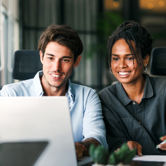 Two colleagues gather around a laptop during a meeting.
