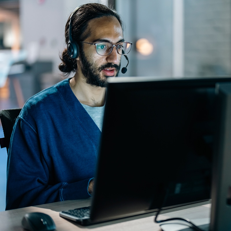 Man wearing headset focused on desktop computer in modern office setting.