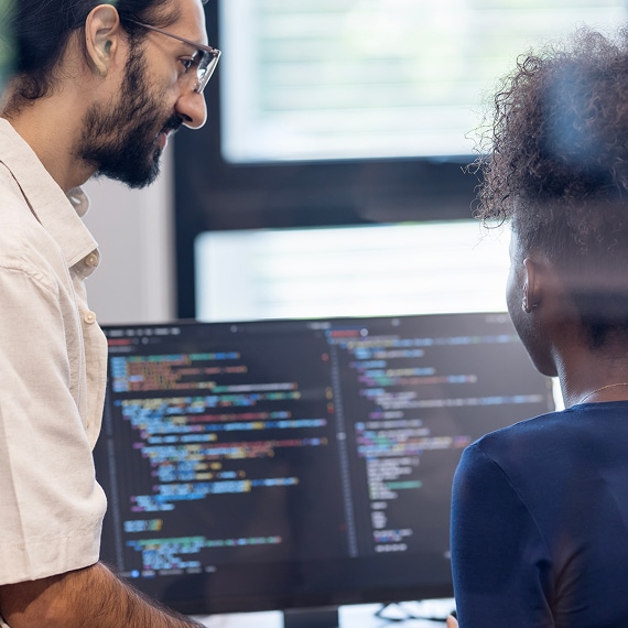 Two colleagues reviewing code together on large desktop monitor.