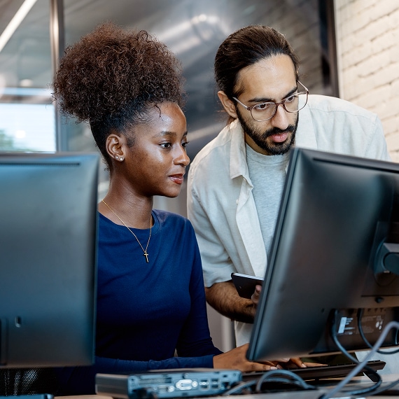 Two coworkers collaborating at dual monitors in contemporary workspace.