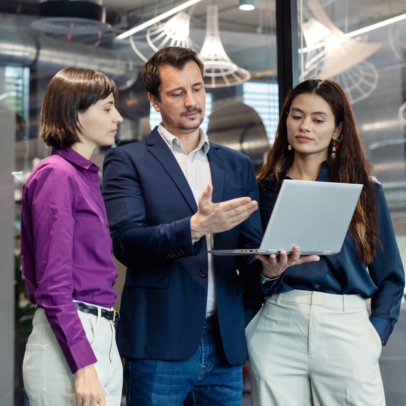 Three colleagues examine analytics on a laptop, aligning governance controls with AI deployment strategy.