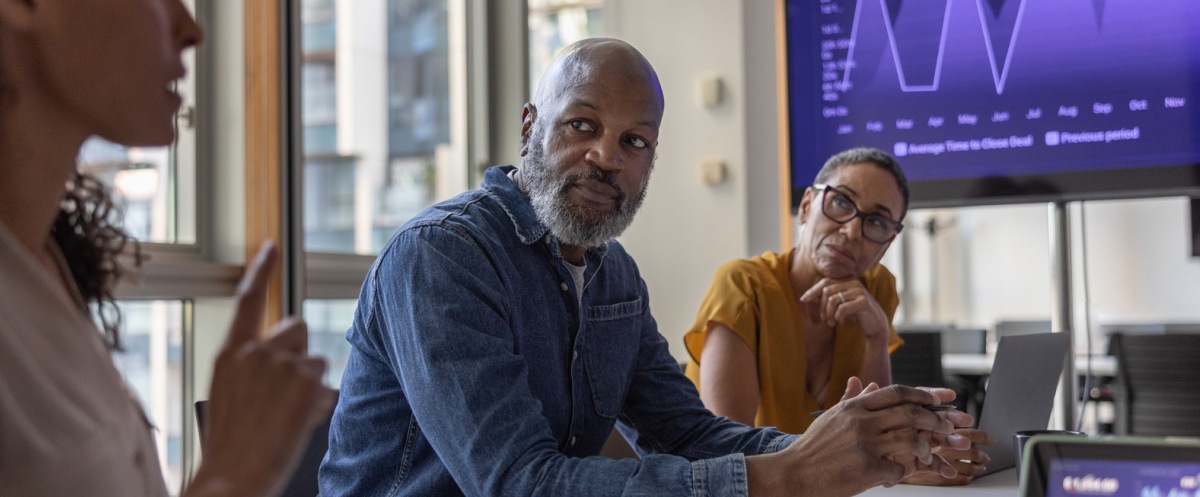 Colleagues discuss business data displayed on screens during a meeting.