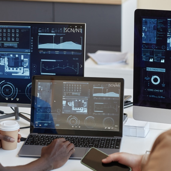 Colleagues analyze technical dashboards across multiple computer screens.