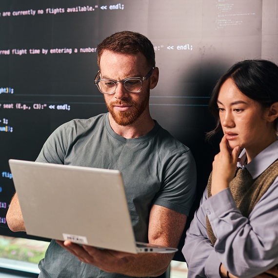 Two colleagues analyzing information together on laptop in office setting.