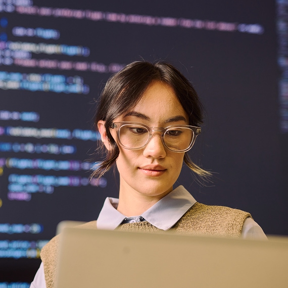 Professional concentrating on laptop with programming code displayed behind.
