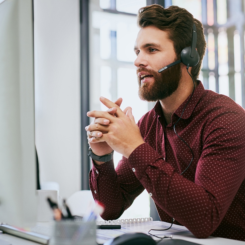 Customer support specialist speaking through headset at office desk.