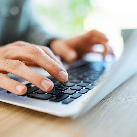 Close-up of hands typing on a laptop keyboard in a bright workspace.