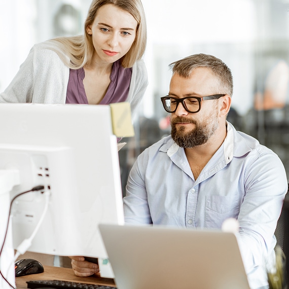 Two colleagues collaborating while reviewing content on a desktop monitor.