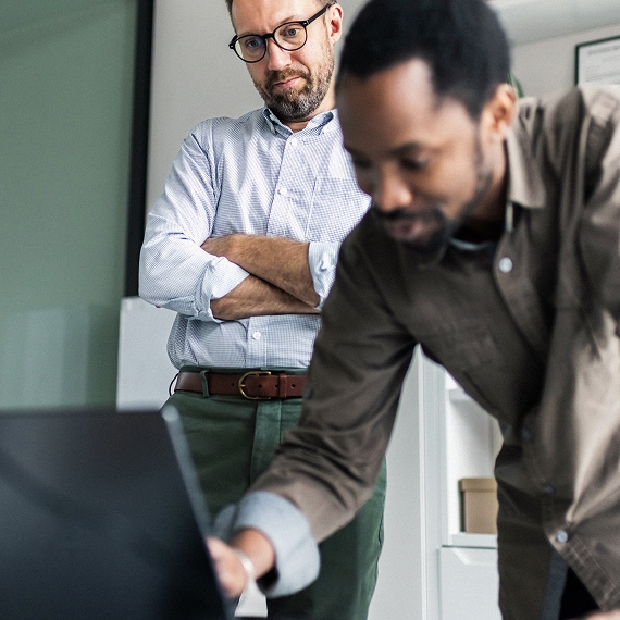 Team members reviewing work on a laptop, with one standing and observing progress.