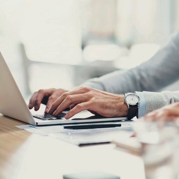 Close-up of hands typing on a laptop beside documents on a desk.