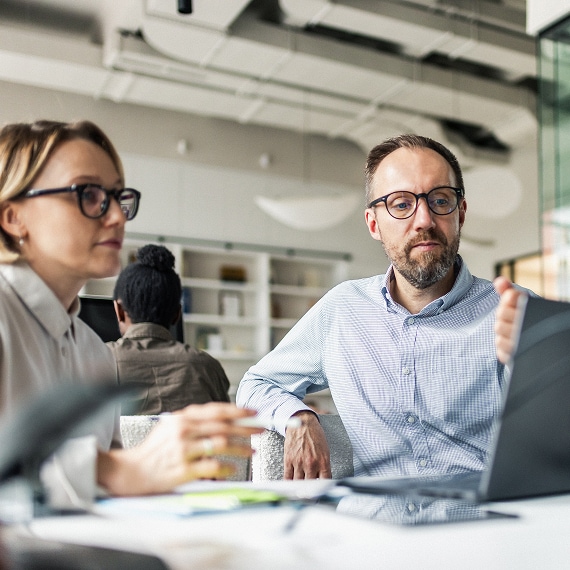 Two professionals focused on a laptop screen during a collaborative office discussion.
